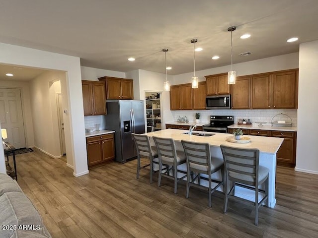 kitchen featuring a center island with sink, appliances with stainless steel finishes, decorative light fixtures, a breakfast bar, and sink