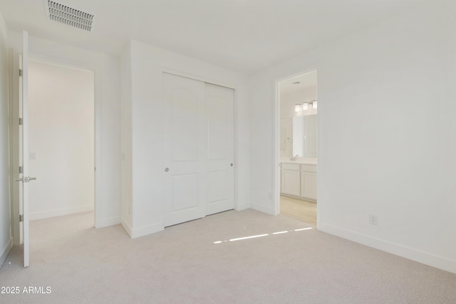 unfurnished bedroom with ensuite bathroom, a closet, and light colored carpet