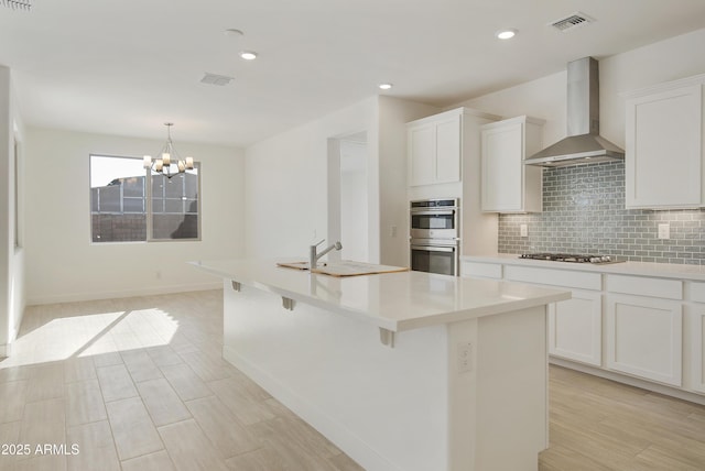 kitchen with stainless steel appliances, white cabinetry, wall chimney exhaust hood, and sink