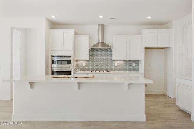 kitchen with white cabinetry, a center island with sink, stainless steel appliances, and wall chimney range hood