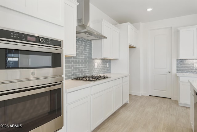 kitchen featuring white cabinets, light hardwood / wood-style flooring, wall chimney exhaust hood, and stainless steel appliances