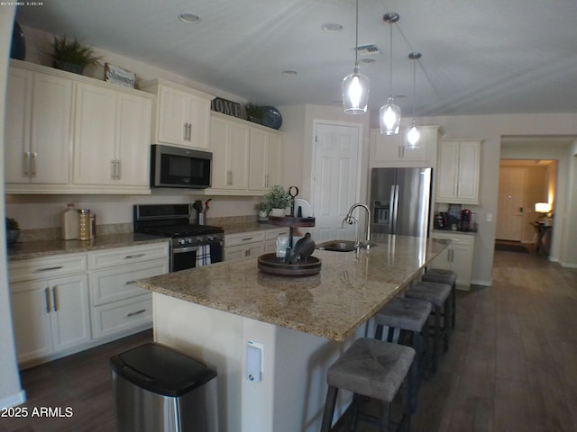 kitchen featuring appliances with stainless steel finishes, pendant lighting, white cabinets, and a center island with sink