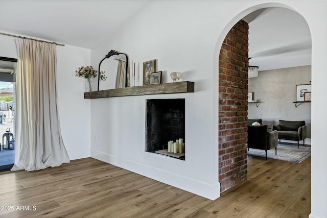interior space featuring arched walkways, lofted ceiling, wood finished floors, and baseboards