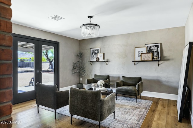 living area featuring an inviting chandelier, wood-type flooring, visible vents, baseboards, and french doors