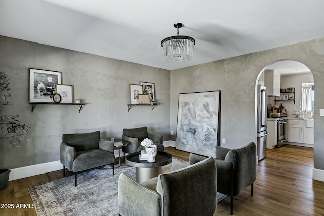 living area featuring wood finished floors, baseboards, a chandelier, and arched walkways