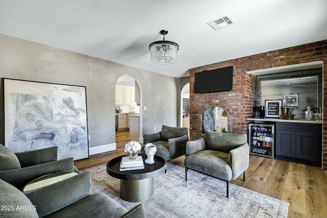 living room with arched walkways, wine cooler, light wood-style flooring, visible vents, and a dry bar