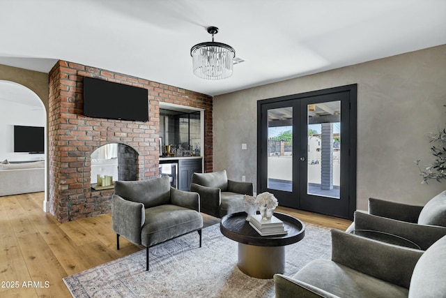 interior space with wine cooler, arched walkways, an inviting chandelier, light wood-type flooring, and french doors