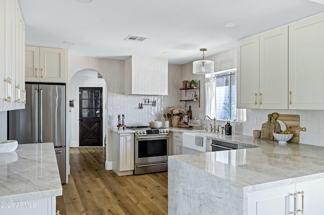 kitchen with arched walkways, stainless steel appliances, light wood-style floors, a sink, and a peninsula