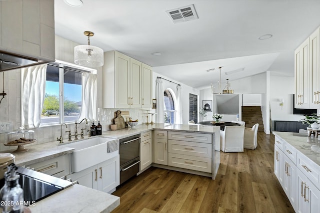 kitchen featuring light stone counters, vaulted ceiling, backsplash, visible vents, and a peninsula