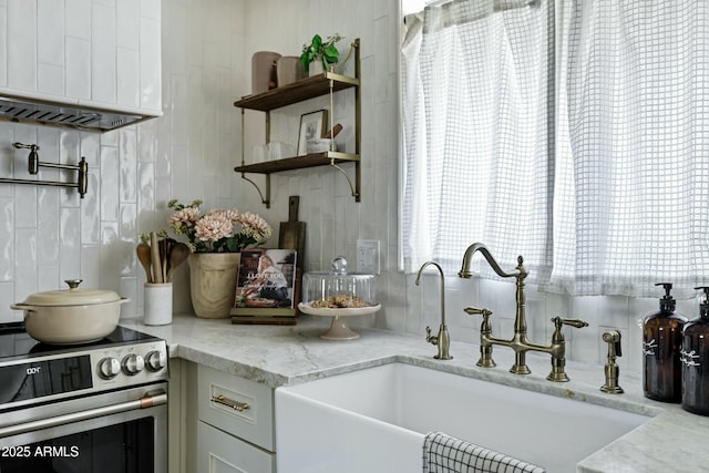 kitchen with light stone counters, tasteful backsplash, white cabinets, a sink, and stainless steel range with electric stovetop