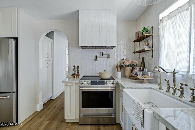 kitchen with light stone countertops, a sink, stainless steel appliances, white cabinetry, and wood finished floors