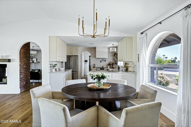 dining room with light wood-style flooring, baseboards, an inviting chandelier, arched walkways, and vaulted ceiling