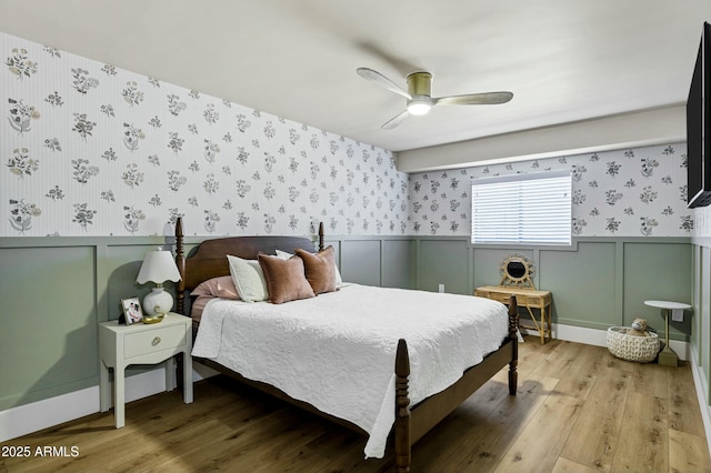 bedroom with wallpapered walls, wainscoting, light wood-style floors, and a decorative wall