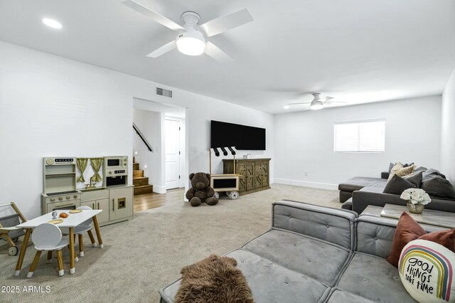 carpeted living room with stairway, visible vents, ceiling fan, and baseboards