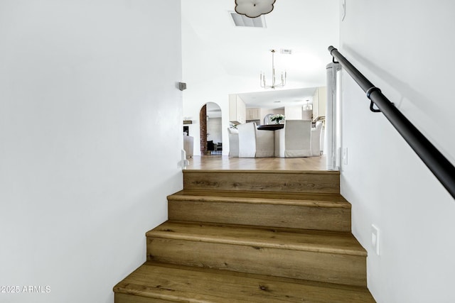 stairway with an inviting chandelier, visible vents, and arched walkways