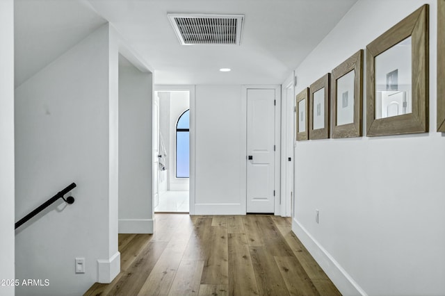 hallway with baseboards, visible vents, an upstairs landing, and wood-type flooring