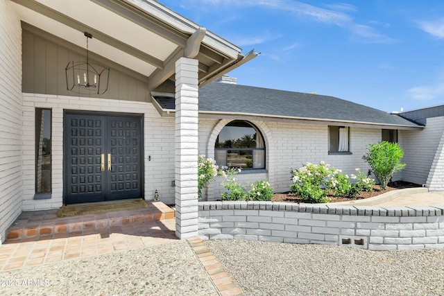 view of exterior entry with roof with shingles and brick siding