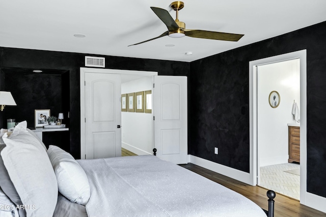 bedroom featuring ensuite bath, a ceiling fan, visible vents, baseboards, and wood finished floors