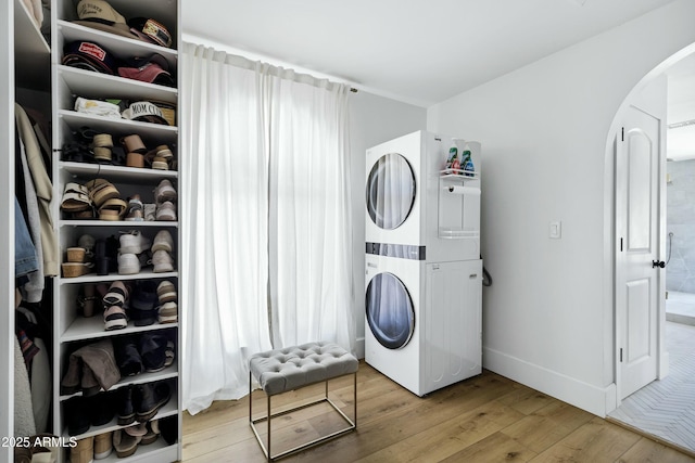 laundry area with wood finished floors, arched walkways, stacked washer / drying machine, laundry area, and baseboards
