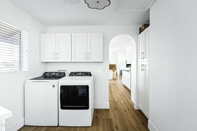 washroom with cabinet space, separate washer and dryer, visible vents, arched walkways, and wood finished floors
