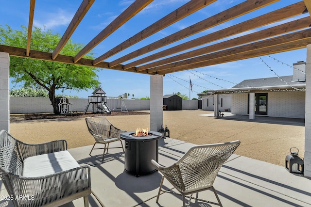 view of patio with an outdoor structure, a fenced backyard, a shed, a playground, and a fire pit