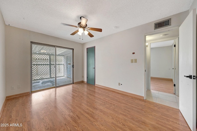 spare room featuring a textured ceiling, light wood finished floors, visible vents, and a ceiling fan