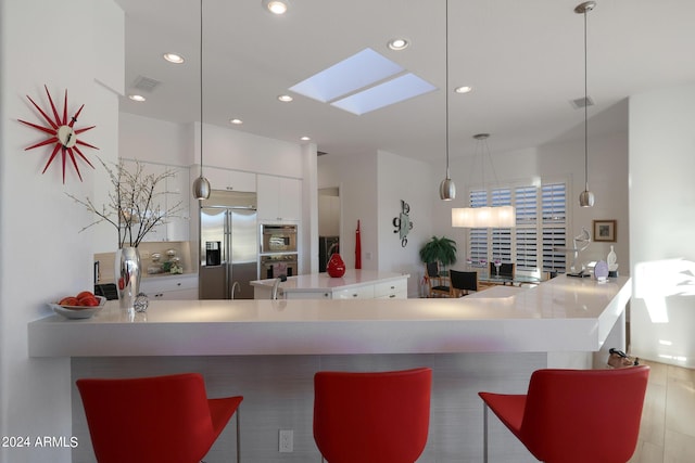 kitchen featuring a skylight, hanging light fixtures, stainless steel appliances, kitchen peninsula, and white cabinets