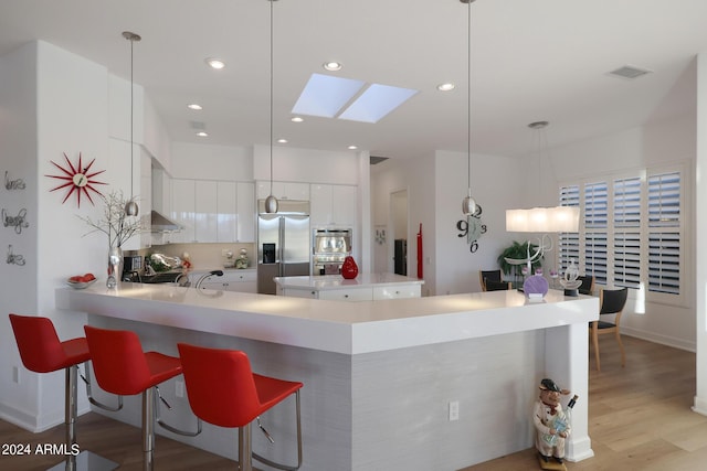 kitchen featuring a skylight, light hardwood / wood-style flooring, decorative light fixtures, white cabinets, and appliances with stainless steel finishes