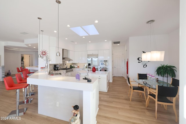 kitchen with wall chimney range hood, kitchen peninsula, hanging light fixtures, stainless steel refrigerator with ice dispenser, and white cabinetry