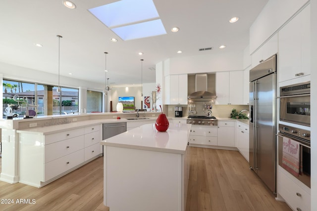 kitchen featuring a skylight, stainless steel appliances, wall chimney range hood, kitchen peninsula, and pendant lighting