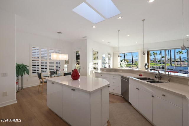 kitchen with dishwasher, sink, a skylight, a kitchen island, and white cabinetry