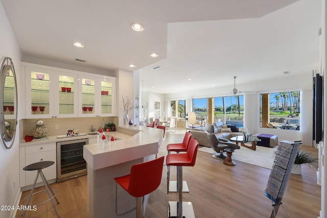 kitchen with a breakfast bar, kitchen peninsula, wine cooler, tasteful backsplash, and white cabinetry