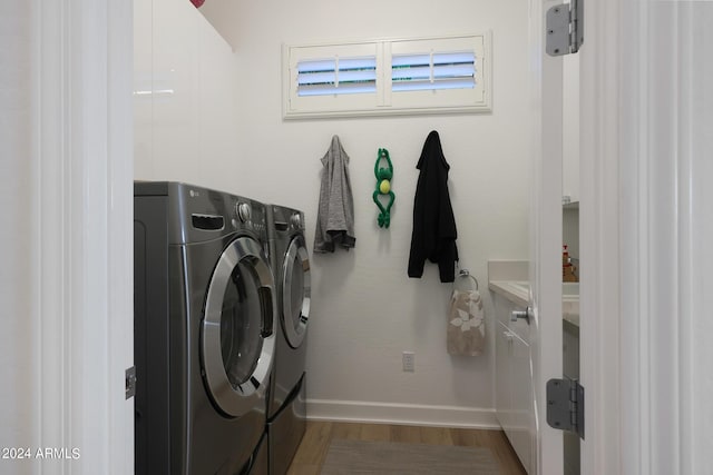 laundry area featuring washing machine and clothes dryer, hardwood / wood-style floors, and cabinets