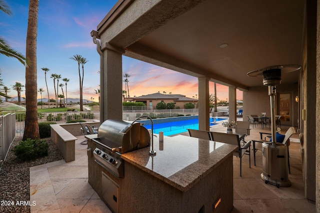 patio terrace at dusk with a fenced in pool, area for grilling, and a grill