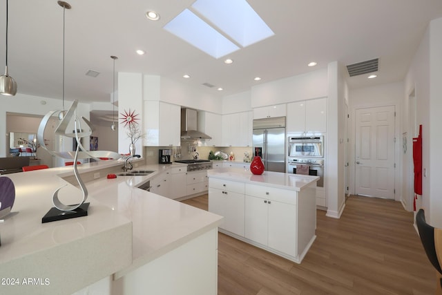 kitchen featuring wall chimney range hood, sink, hanging light fixtures, a skylight, and stainless steel appliances