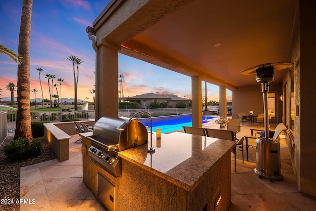 patio terrace at dusk with a fenced in pool, exterior kitchen, and grilling area