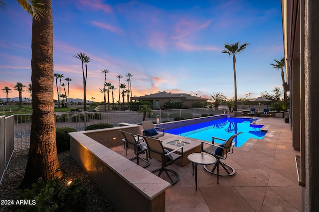 pool at dusk with a fire pit and a patio area