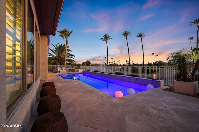 pool at dusk with a patio and a water view