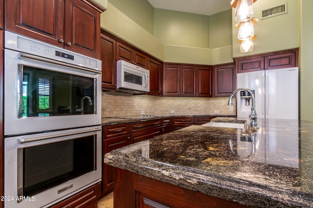 kitchen featuring tasteful backsplash, dark stone countertops, a towering ceiling, and stainless steel appliances