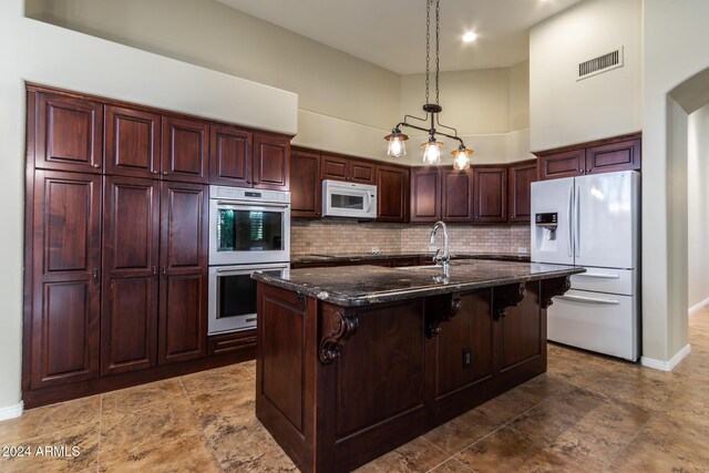 kitchen featuring a breakfast bar, white appliances, backsplash, an island with sink, and decorative light fixtures