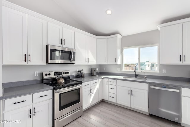 kitchen with sink, white cabinetry, vaulted ceiling, light wood-type flooring, and appliances with stainless steel finishes