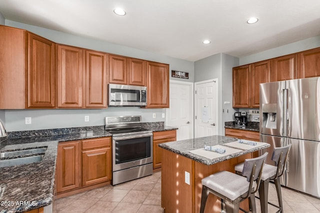 kitchen featuring a breakfast bar, a sink, appliances with stainless steel finishes, a center island, and dark stone countertops