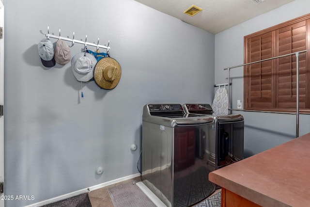 clothes washing area with laundry area, visible vents, baseboards, tile patterned floors, and washing machine and dryer