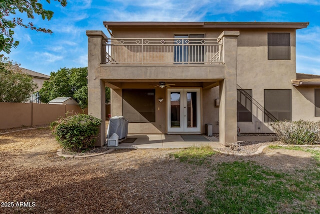 rear view of house featuring a balcony, ceiling fan, fence, french doors, and stucco siding