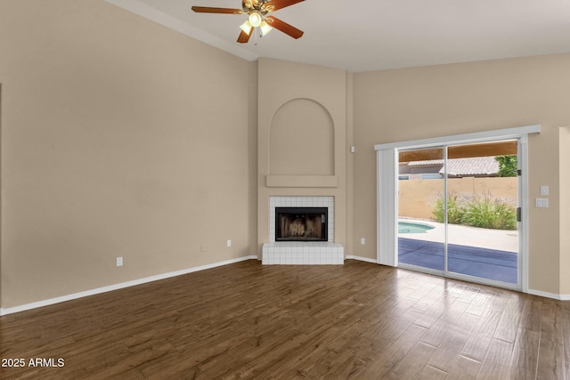 unfurnished living room with ceiling fan, a tiled fireplace, baseboards, vaulted ceiling, and dark wood-style floors