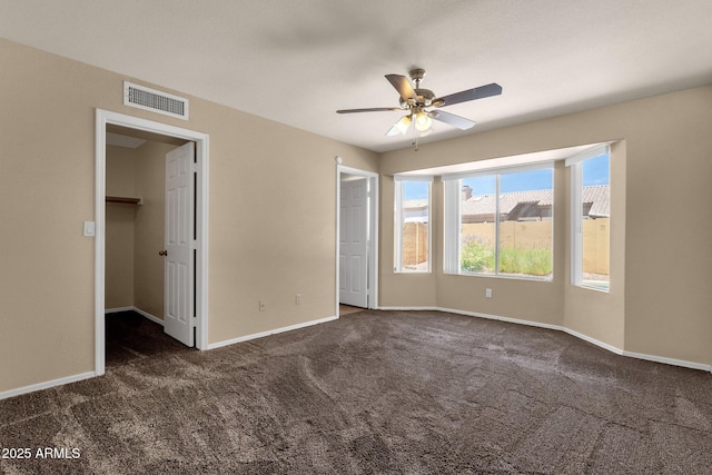 unfurnished bedroom featuring visible vents, baseboards, a walk in closet, a ceiling fan, and carpet
