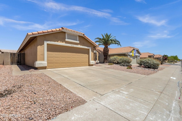 view of front of property featuring a garage, stucco siding, a gate, a tiled roof, and concrete driveway