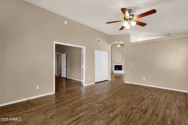 unfurnished room featuring a ceiling fan, a towering ceiling, visible vents, dark wood finished floors, and baseboards