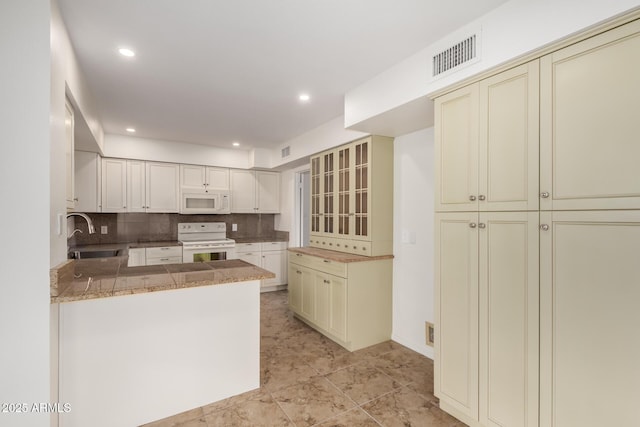 kitchen featuring tasteful backsplash, visible vents, cream cabinets, a sink, and white appliances