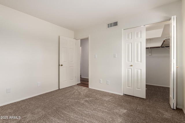 unfurnished bedroom featuring carpet floors, a walk in closet, a closet, visible vents, and baseboards